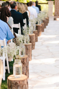 Aisle lined with cut trunks with mason jars & flowers on them